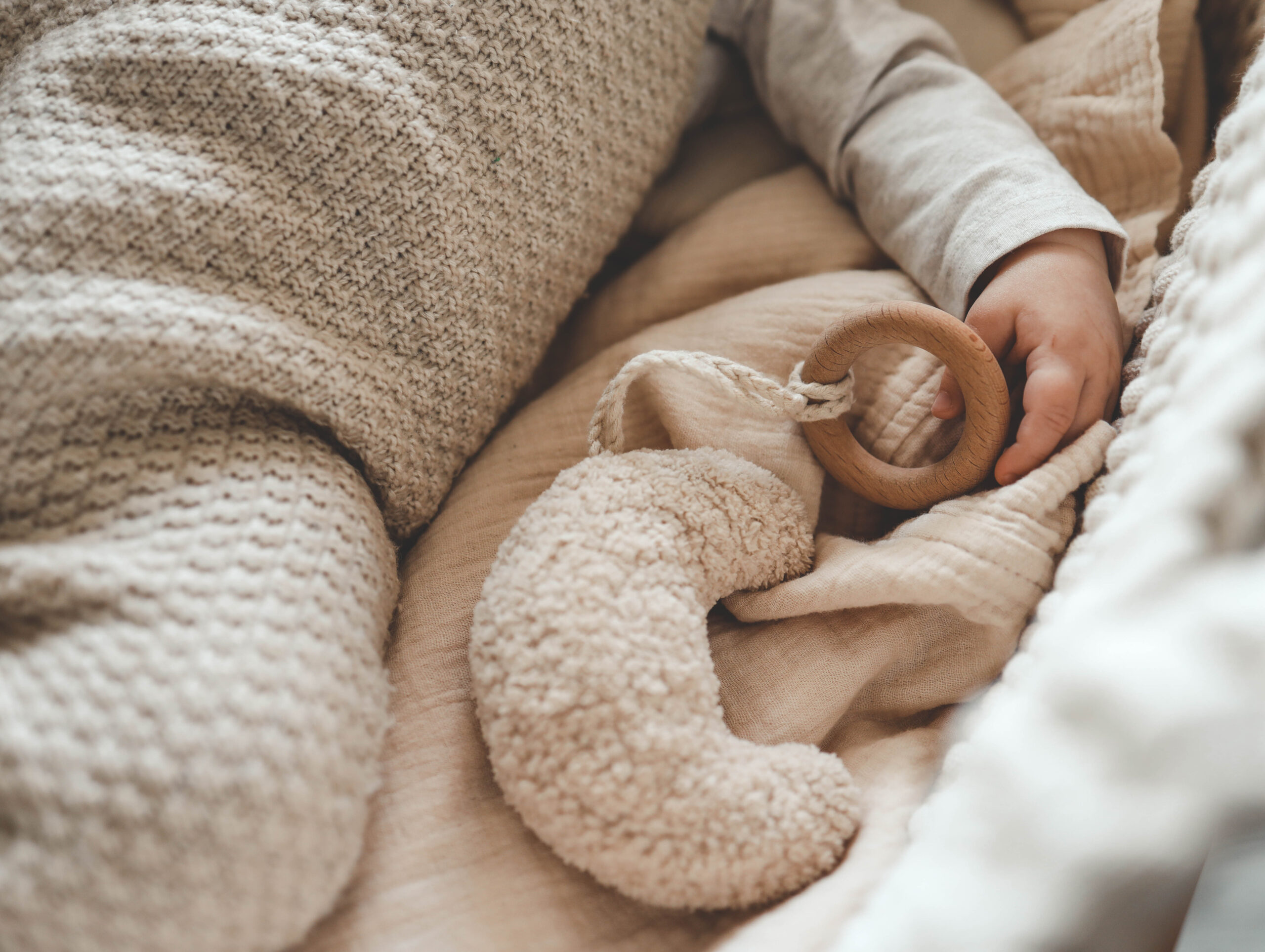 Sleeping baby holding a knitted comforter toy on a cream blanket